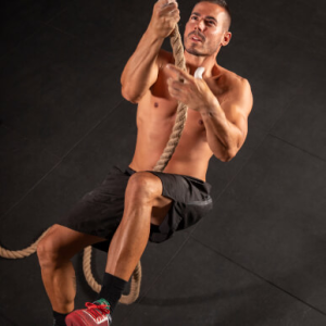 Athlete performing rope climbing exercise for upper body strength and endurance.
